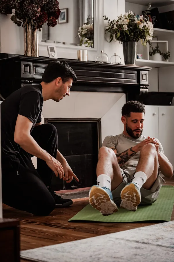 Coach sportif à genoux guidant un exercice doux au sol, dans le salon de son client