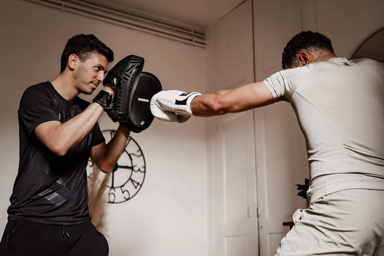 Coach sportif à domicile à Toulouse tenant une patte d'ours pendant une séance de boxe dans le salon de son client