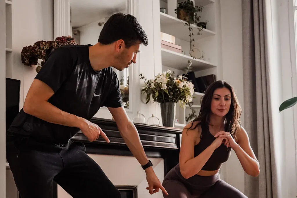 Coach sportif à domicile à Toulouse montrant un squat à une cliente dans son salon