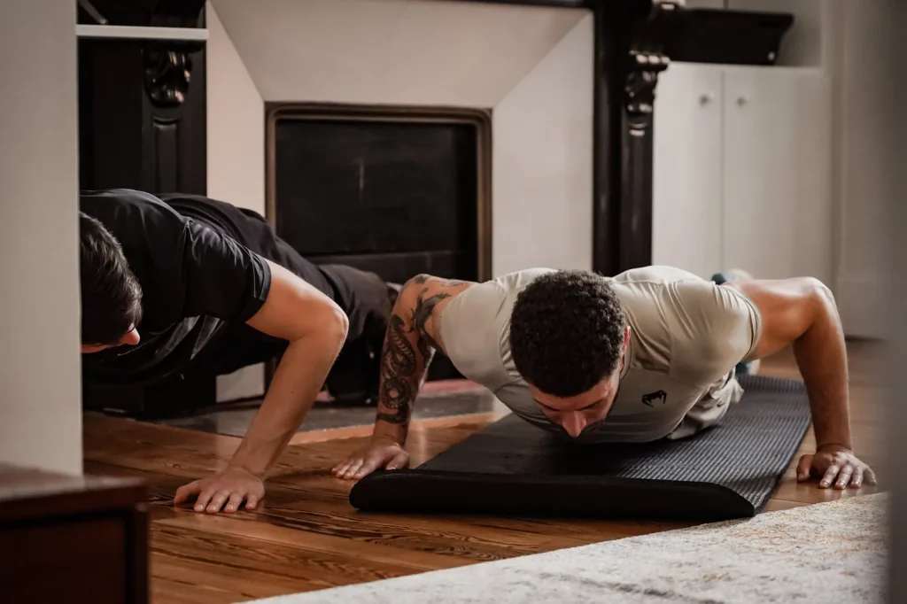 Coach sportif à domicile à Toulouse faisant des pompes à côté de son client, dans le salon, pendant une séance pour perdre du poids