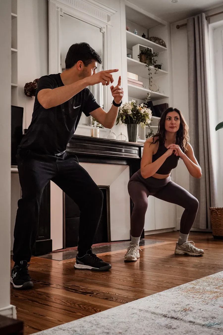 Cliente faisant des squats dans son salon, encouragée par son coach sportif à domicile
